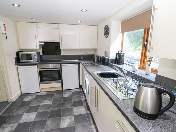 A modern kitchen with white cabinets, a microwave, an oven, a dishwasher, and a kettle. - Hove Wood View (Hebden Bridge)