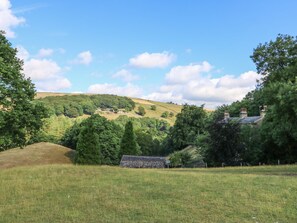A rural landscape with rolling hills, a small house with a thatched roof, and a fenced field. - Hove Wood View (Hebden Bridge)