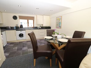A compact kitchen with a washing machine, a dining table with chairs, and a clock on the wall. - Hove Wood View (Hebden Bridge)
