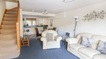 A spacious living area with a staircase, a dining table with chairs, a sofa, and a kitchen in the background.