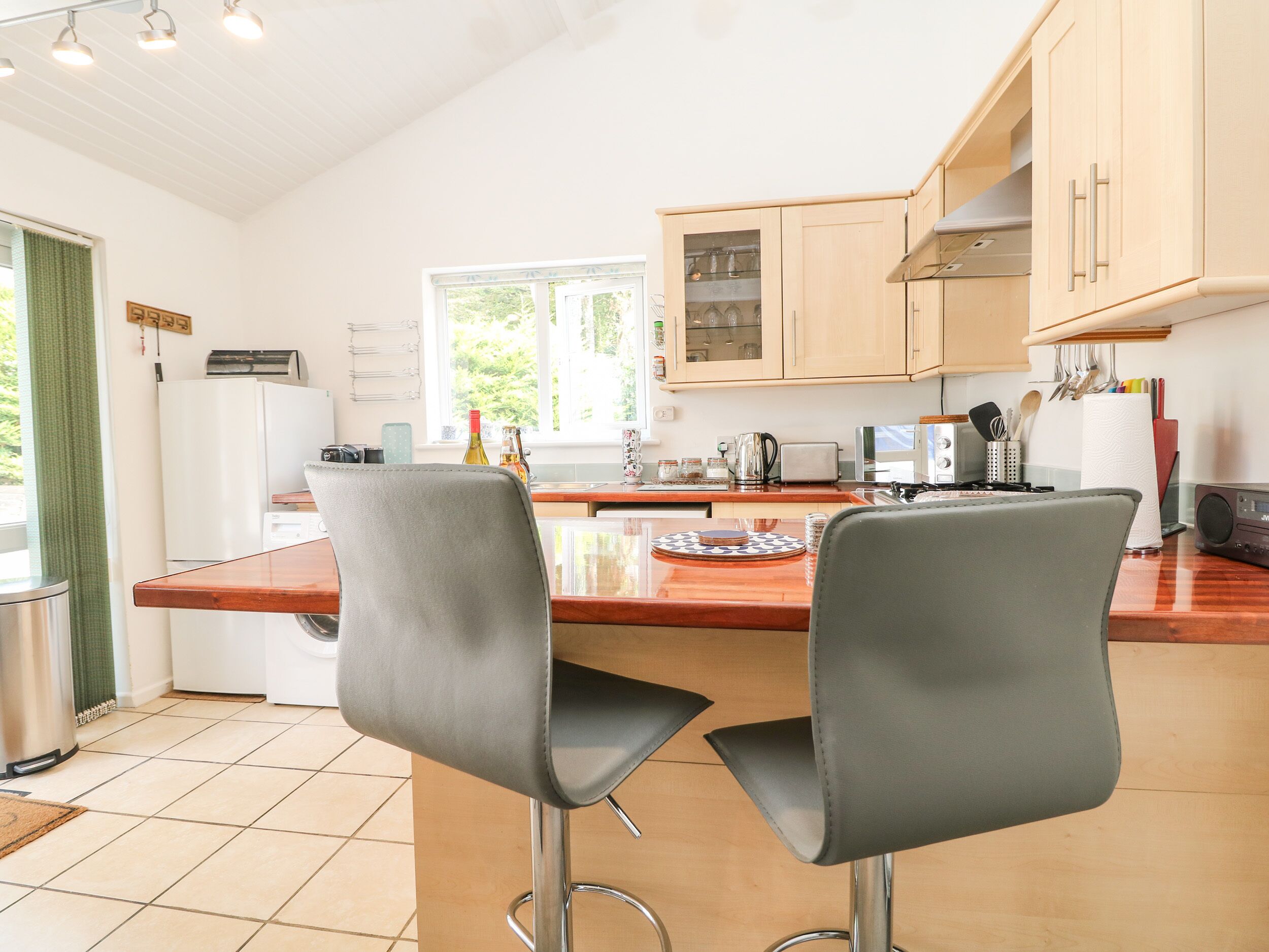Une cuisine moderne avec deux tabourets de bar gris, un îlot central en bois et un réfrigérateur blanc.