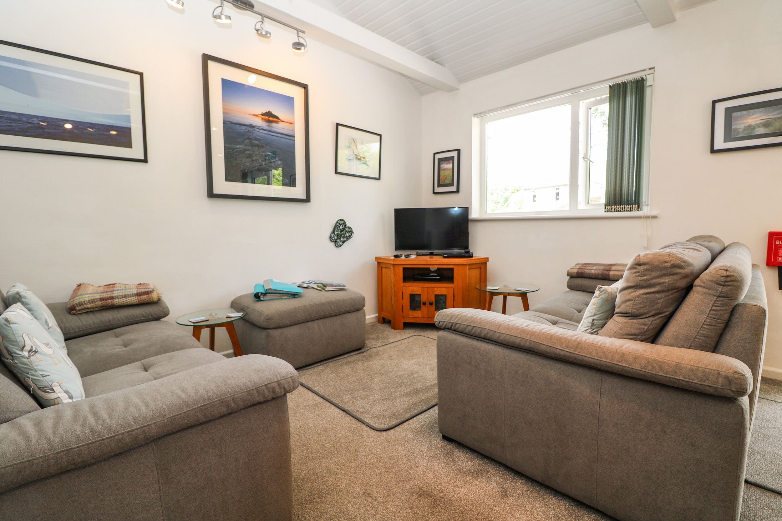 A living room with two grey sofas, a wooden TV stand, and framed pictures on the walls.