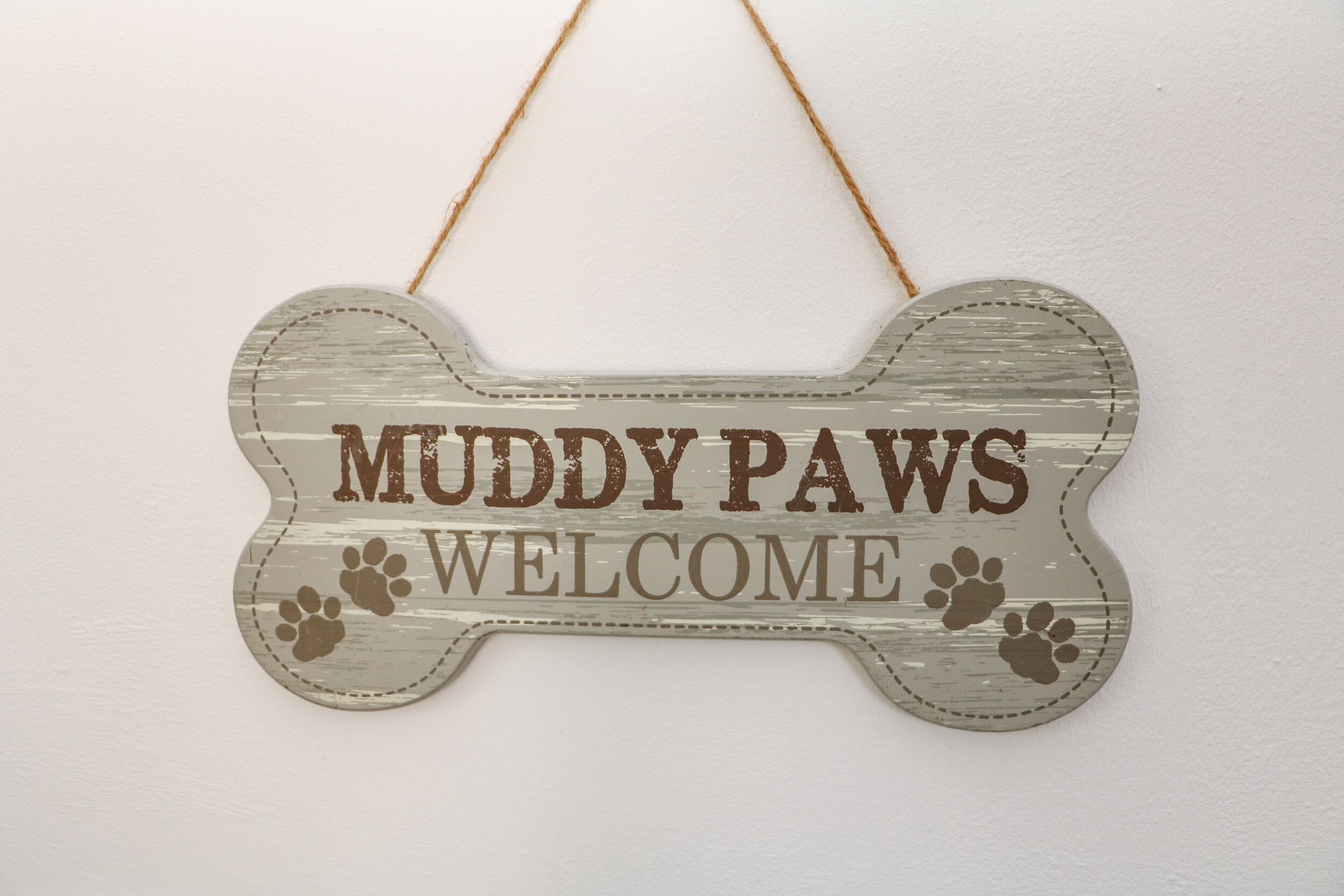 Ein schild in Knochenform mit dem Schriftzug 'Muddy Paws Welcome' und Pfotenabdrücken.