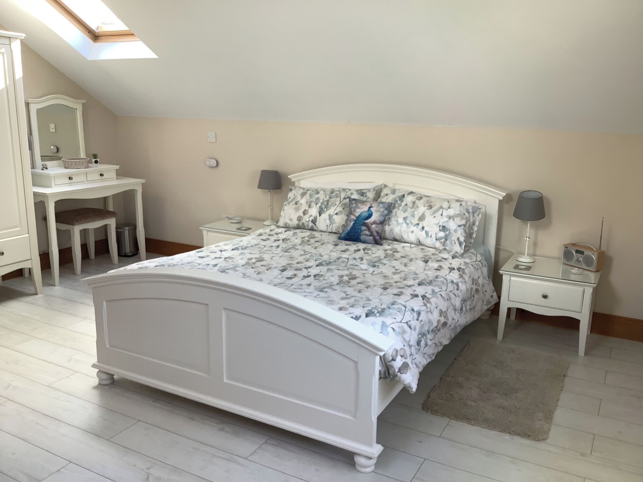 A bedroom with a bed, a desk, a chair, a nightstand, and a lamp.