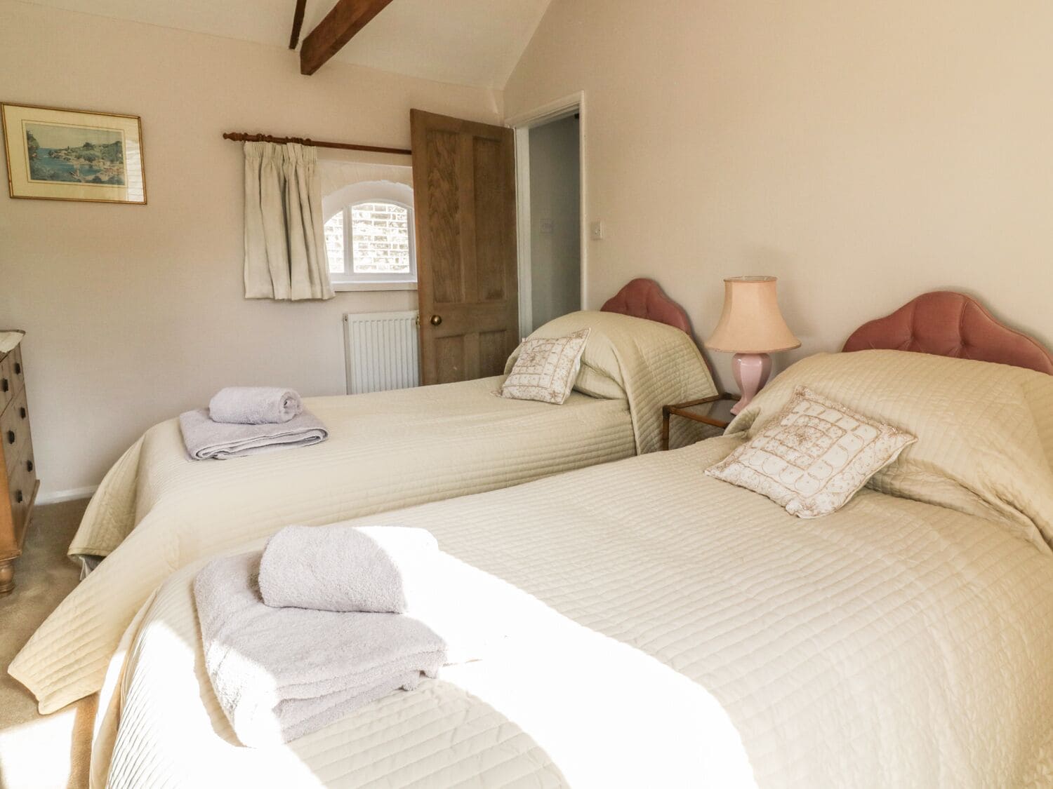 A bedroom with two beds, a wooden door, a lamp, and a framed picture on the wall.