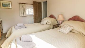 A bedroom with two beds, a wooden door, a lamp, and a framed picture on the wall.