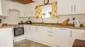 A kitchen with white cabinets, a wooden countertop, a built-in oven, a sink, and a clock on the wall. - Stable Cottage (Sudbury)