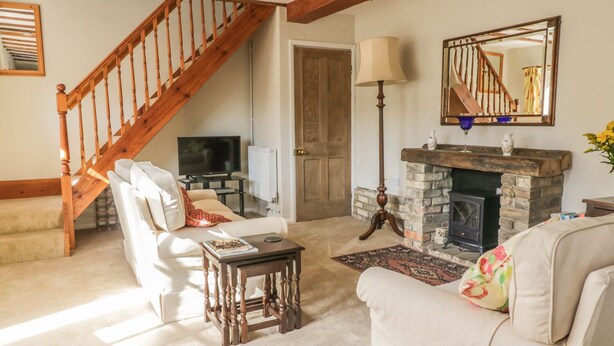 A living room with a fireplace, a television, a sofa, and a staircase. - Stable Cottage (Sudbury)