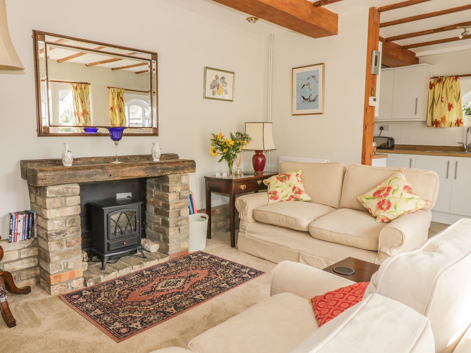A cozy living room with a fireplace, a sofa, a rug, and a kitchen in the background.