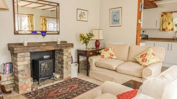 A cozy living room with a fireplace, a sofa, a rug, and a kitchen in the background.