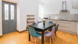 A modern kitchen with a dining area, wooden flooring, and a grey door with stained glass panels. - Westwood (Ballater)