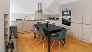 A modern kitchen with a dining area, featuring a central island, built-in oven, and a stainless steel range hood. - Westwood (Ballater)