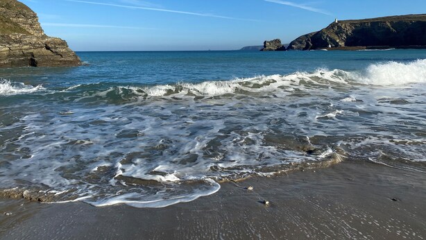 Una playa costera con olas, acantilados rocosos y un faro.