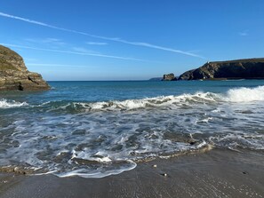 A coastal beach with waves, rocky cliffs, and a lighthouse. - The Chace (Redruth)
