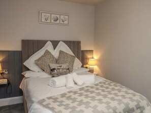 A neatly made bed with a patterned bedspread, pillows, and a decorative pillow with a cityscape design. There are two bedside lamps on either side of the bed. - Archie's Anchor (Scarborough)