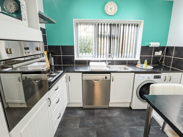 A modern kitchen with white cabinets, a dishwasher, a stove, and a sink.
