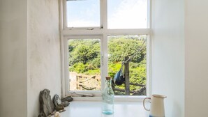 A window with a view of a lush green landscape, a rustic rope swing, and a rustic shelf with a bottle and a mug. - Clevelyn (Saltburn-by-the-Sea)
