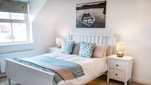 Een slaapkamer met een bed, twee nachtkastjes, een raam en een schilderij aan de muur.