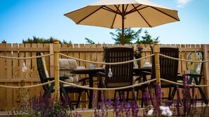 Een terras buiten met een houten schutting, een tafel met stoelen en een parasol.