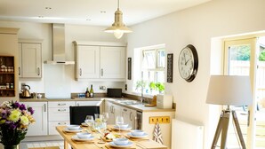 Een moderne keuken met witte kastjes, een eettafel voor vier personen en een schaal fruit op het aanrecht.