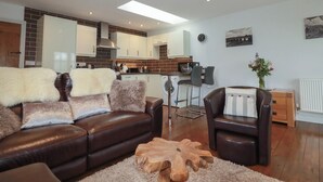 A modern living room with a leather sofa, a wooden coffee table, and a dining area with a kitchen in the background. - The Smithy (Bodmin)