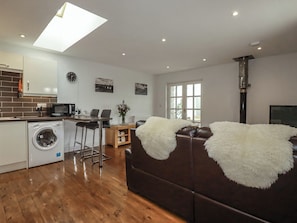 A modern living room with a sofa, a washing machine, a microwave, and a dining area. - The Smithy (Bodmin)