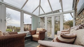 A conservatory with wicker furniture, a glass door leading outside, and a view of the garden. - The Smithy (Bodmin)