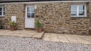 A stone building with a white door, two windows, and potted plants. - The Smithy (Bodmin)