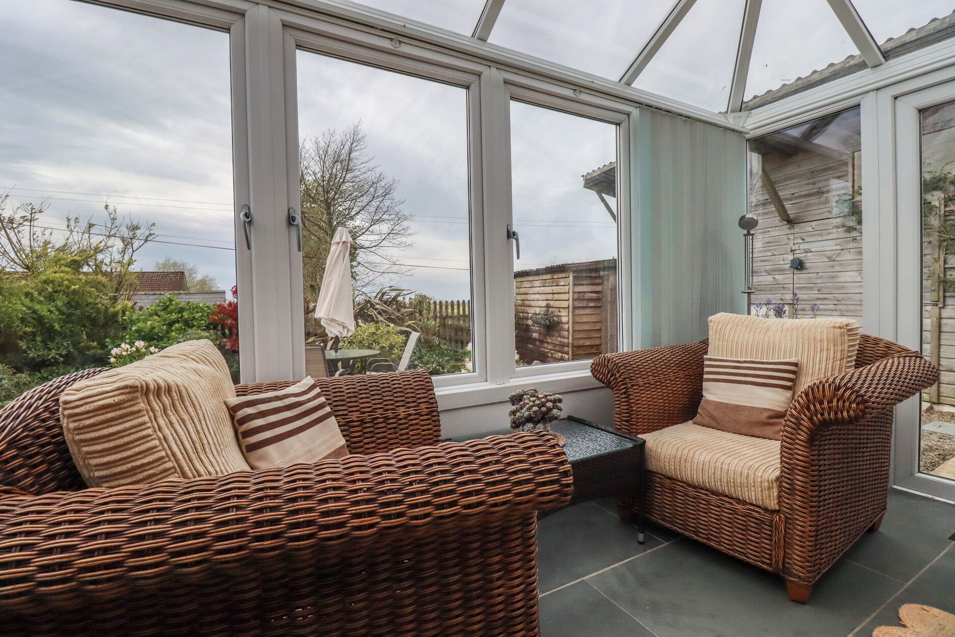 A conservatory with wicker furniture and a view of the garden.
