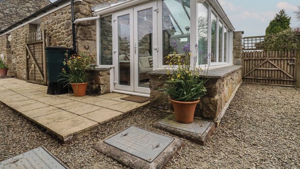A stone house with a glass conservatory, potted plants, and a gravel driveway. - The Smithy (Bodmin)