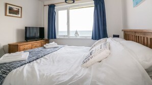 Ein Hotelzimmer mit Bett, Fernseher auf einer Holzkommode, einem Fenster mit Vorhängen und einem Bild an der Wand.