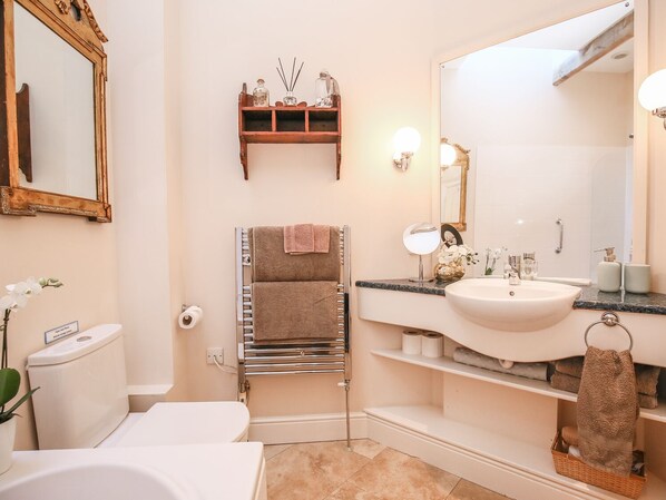 Un baño moderno con inodoro, lavamanos y bañera. Hay un perchero con toallas, un espejo y un estante con artículos de aseo.
