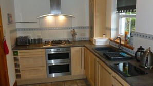 A compact kitchen with a gas stove, two ovens, a sink, and a window with a view. - Sidhean Dubha Holiday Home (Portree)