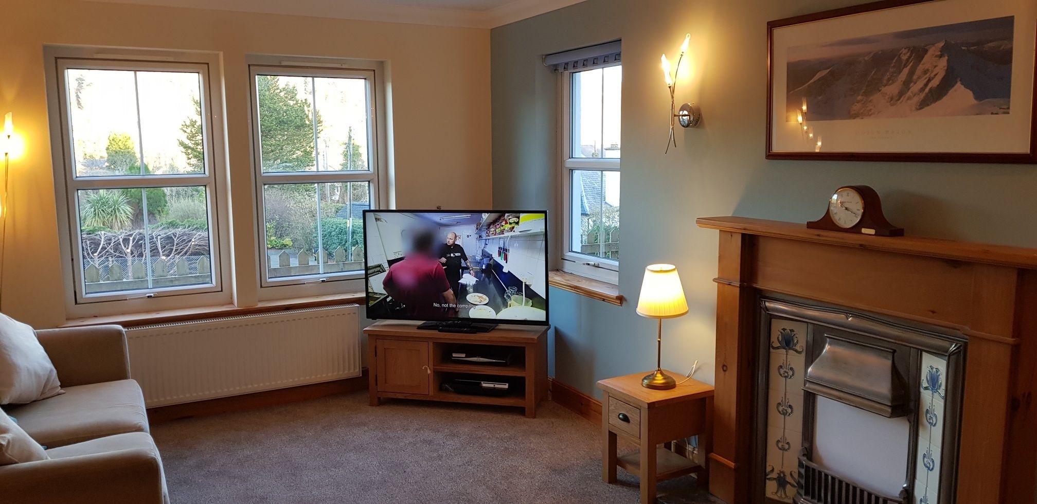 Ein Wohnzimmer mit Fernseher, Kamin und großen Fenstern.