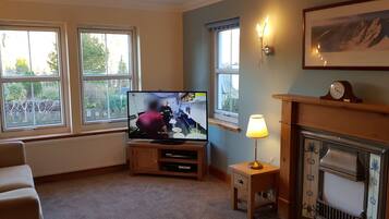 Ein Wohnzimmer mit Fernseher, Kamin und großen Fenstern.