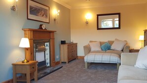 A cozy living room with a fireplace, a sofa, and a coffee table. - Sidhean Dubha Holiday Home (Portree)