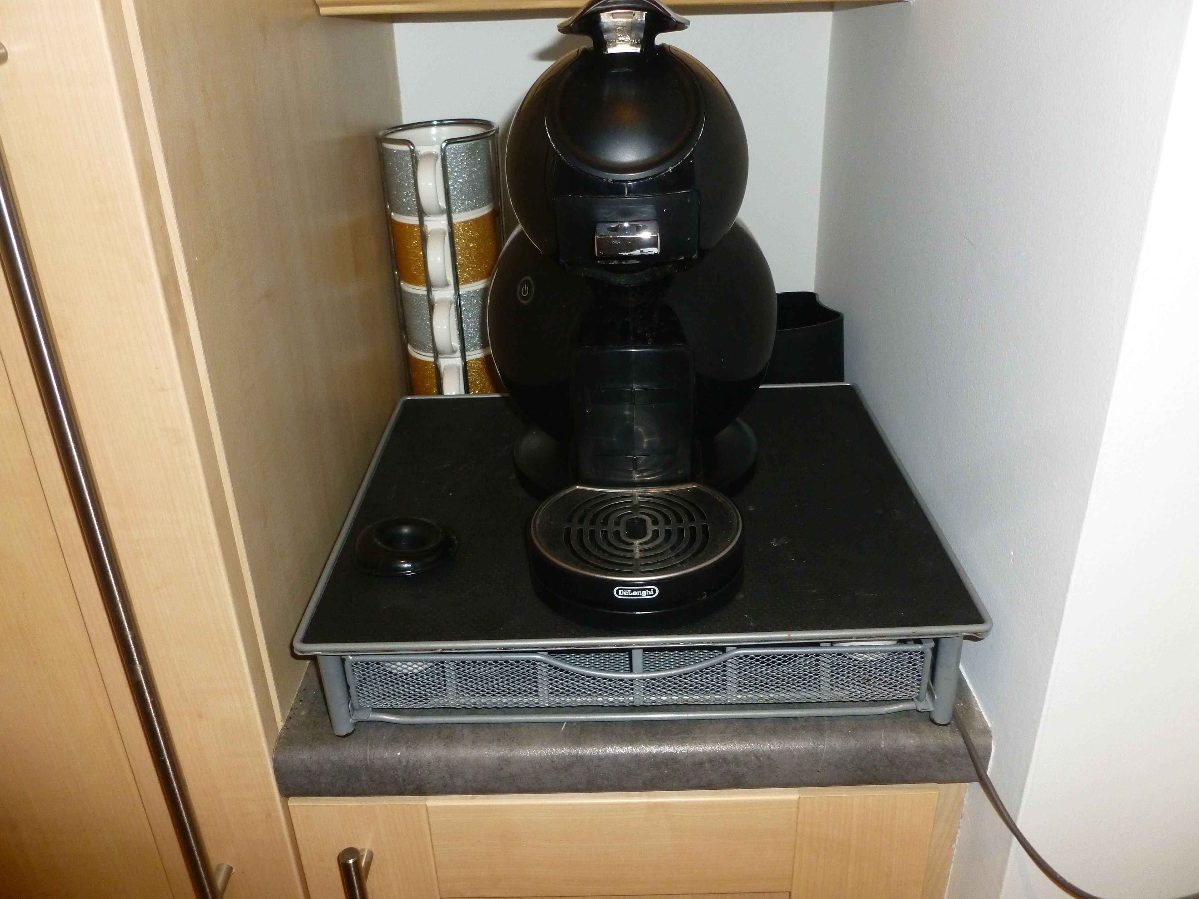 A coffee maker on a countertop with a mesh vent, a canister, and a cabinet below.