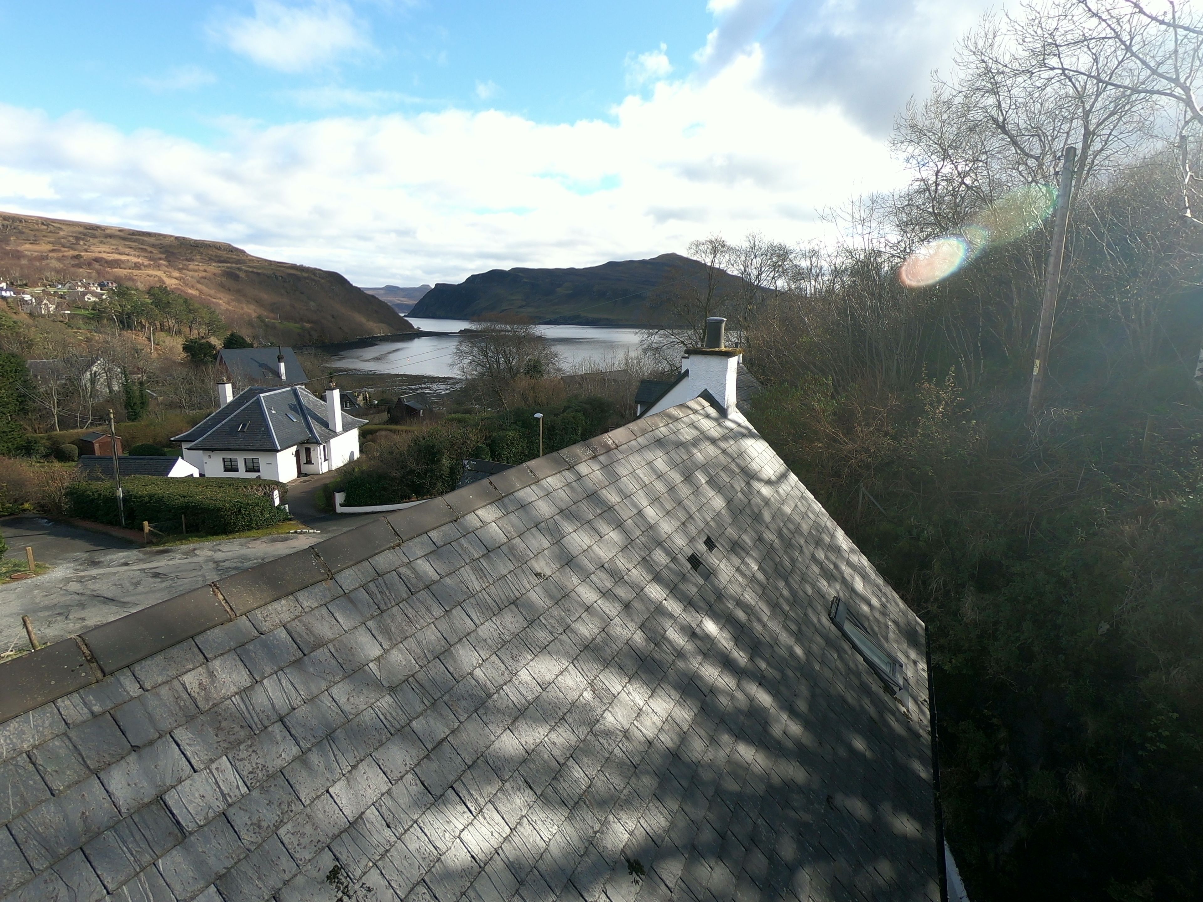 A view of a residential area with a house, a paved driveway, and a river in the background.