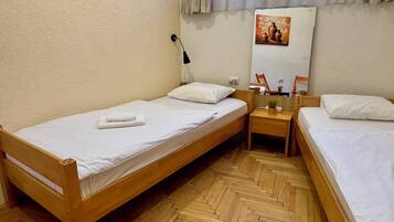 Une petite chambre propre et bien rangée, avec deux lits en bois, une table de chevet en bois sur laquelle se trouve une lampe, et un miroir accroché au mur.