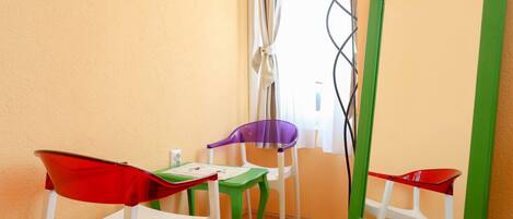 A room with a green-framed mirror, a white chair, a purple chair, and a red chair.