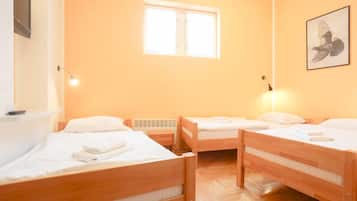 A room with three wooden beds, a window, a wall-mounted picture, and a bedside lamp.