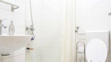 Un baño con ducha, inodoro, lavabo y un escalón pequeño con un tapete verde.