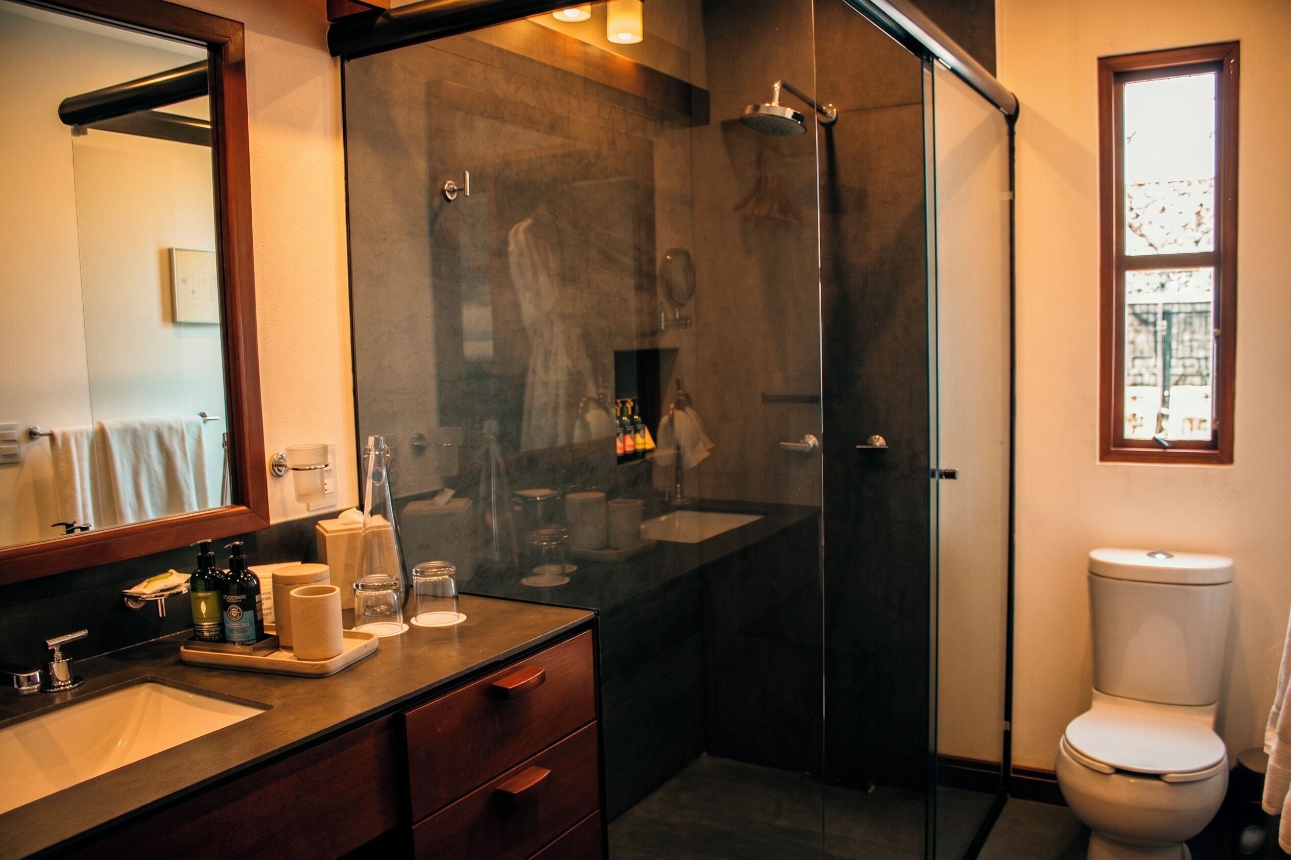 Un bagno moderno con cabina doccia in vetro, uno specchio grande, un lavandino con articoli da toilette e un water.