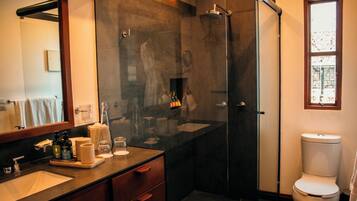 Un bagno moderno con cabina doccia in vetro, uno specchio grande, un lavandino con articoli da toilette e un water.