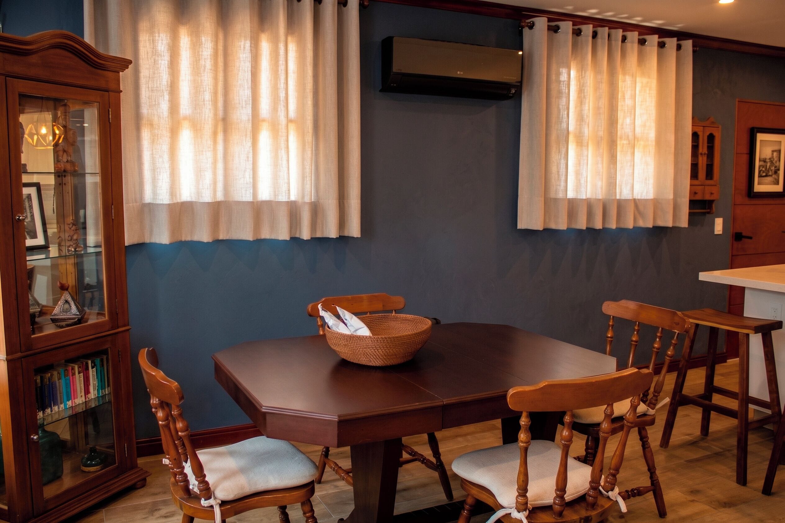 Una zona pranzo con tavolo in legno, quattro sedie, un cesto di vimini e un mobile con ante in vetro.