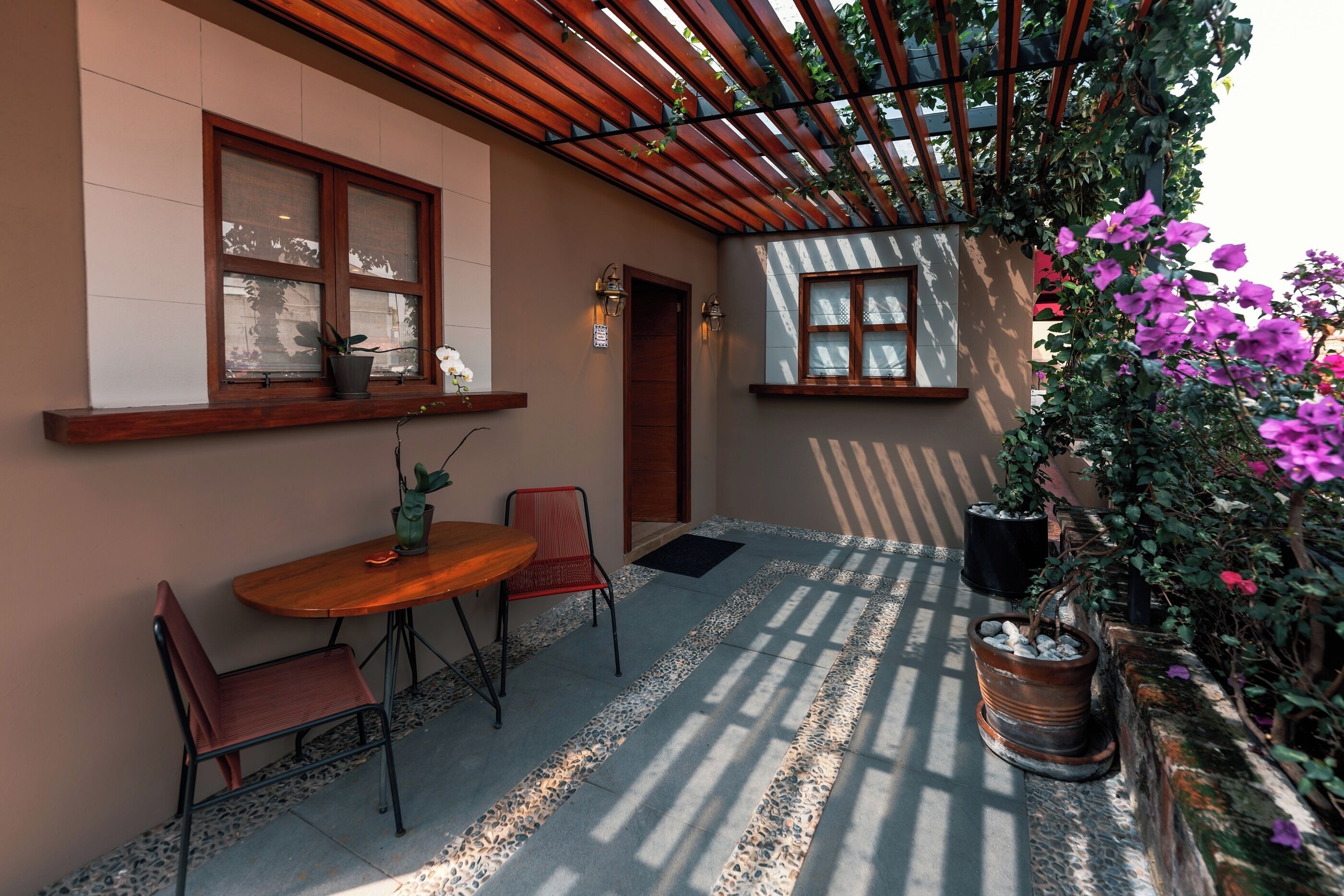 A patio with a wooden table and chairs, potted plants, and a pergola structure.