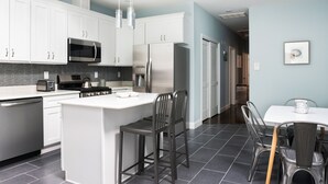 A modern kitchen with white cabinets, stainless steel appliances, and a central island with bar stools. - Giles Ave 6 Bedroom Gem (Jersey City)