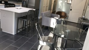 A modern kitchen with a central island, stainless steel appliances, and a glass dining table with metal chairs. - Giles Ave 6 Bedroom Gem (Jersey City)