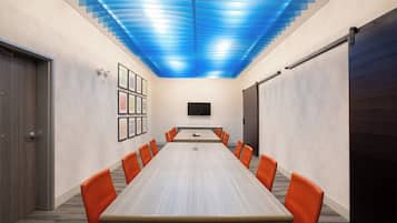 A conference room with a long table, orange chairs, a flat-screen TV, and a blue ceiling design.