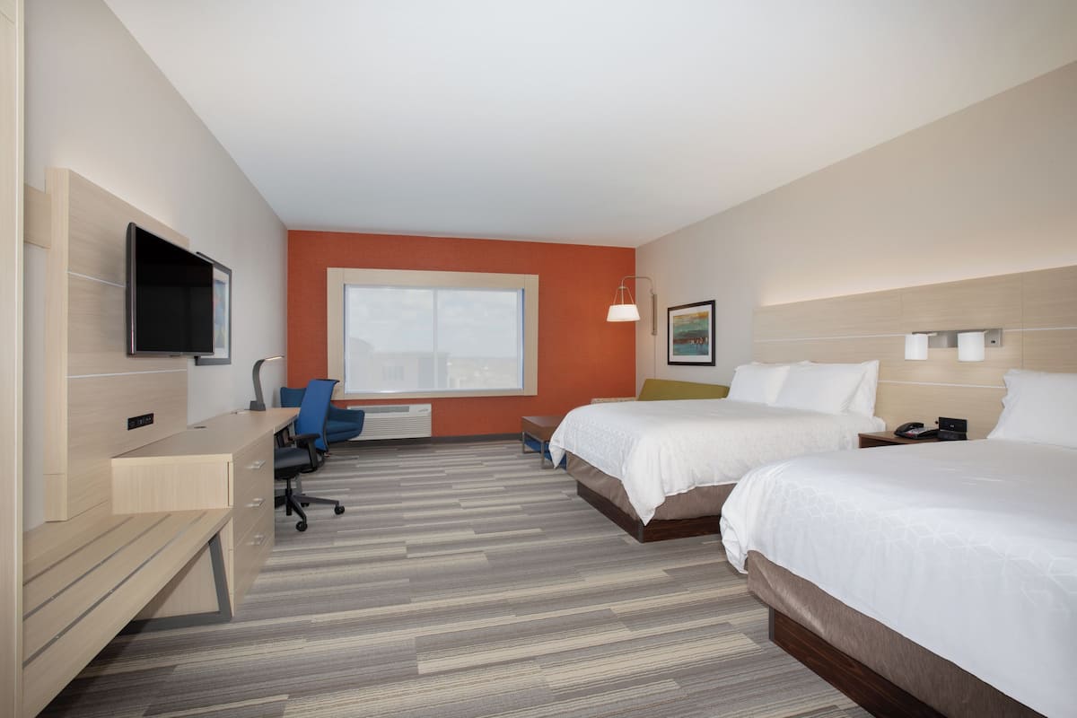 A hotel room with two beds, a desk, a chair, a TV, and a window.
